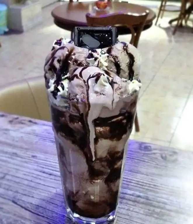 دسر لذیذ بستنی شکلاتی یا میلک شیک غلیظ در لیوانی بزرگ، تزئین شده با سس شکلات و خامه، از منوی جذاب کافه فراز.