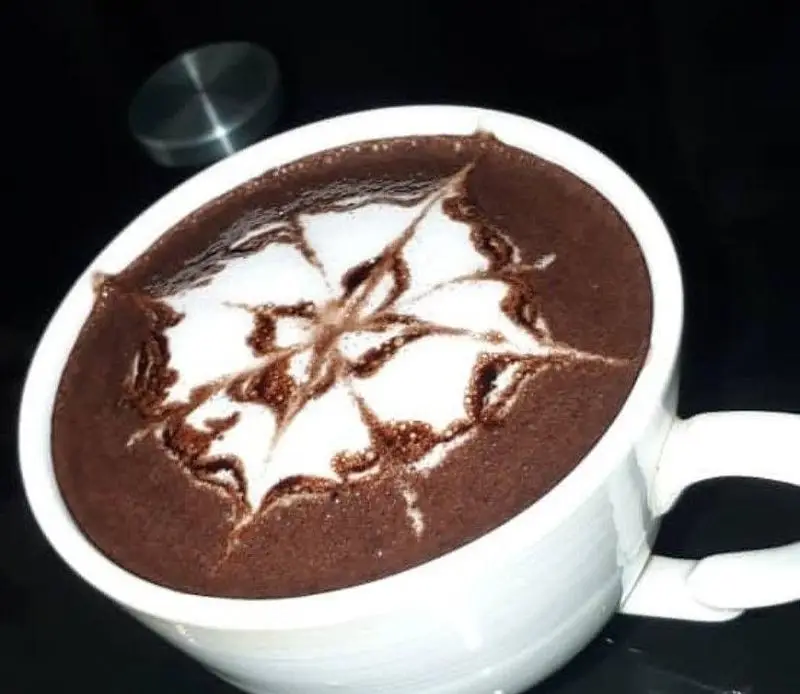 هات چاکلت دلچسب کافه فراز در ماگی سفید با لاته آرت هنرمندانه و طرحی زیبا روی فوم. نوشیدنی گرم و شکلاتی لذت‌بخش.