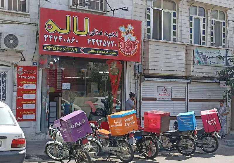 نمای بیرونی کترینگ و تهیه غذای لاله با تابلو قرمز، شماره تلفن‌ها و موتورهای پیک آماده ارسال غذا از طریق اسنپ اکسپرس و میان.