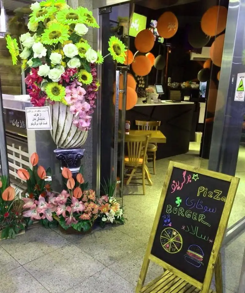 ورودی دکور شده رستوران فست فود برگرینو با تابلو گچی تبلیغ پیتزا، برگر و سالاد. دکوراسیون داخلی با بادکنک و گلدان گل.