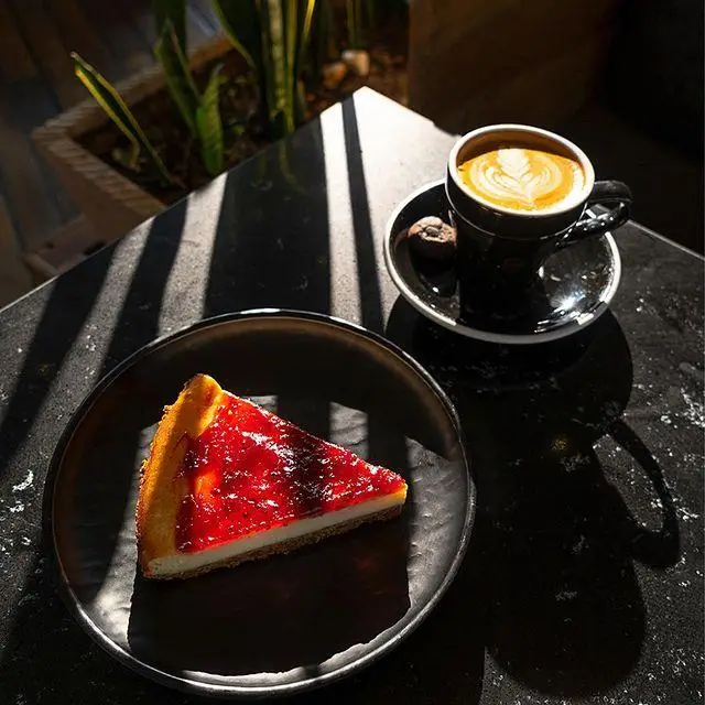 برش چیزکیک توت‌فرنگی و فنجان قهوه با لاته آرت زیبا، در کافه رستوران لول ۴. تجربه‌ی دسر و نوشیدنی در فضایی دنج و آفتابی.