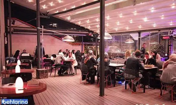 تصویری از کافه رستوران لول ۴ در شب، با فضای باز روشن و سقف متحرک، مشتریانی مشغول گفت‌وگو و صرف غذا در محیطی گرم و دوستانه.