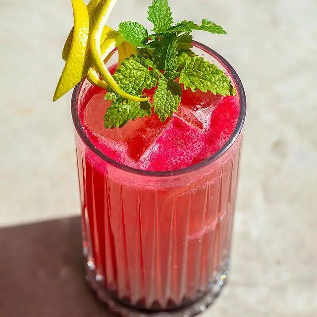 یک کوکتل صورتی/قرمز خنک و تازه در لیوان بلند، با تکه‌های یخ، برگ‌های نعناع و پوست لیمو. نوشیدنی‌های کافه رستوران لول ۴.