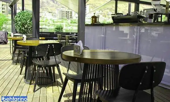 فضای باز دنج کافه رستوران لول ۴ با میز و صندلی‌های شیک چوبی و منظره‌ای دلنشین از شهر و کوهستان، ایده‌آل برای صرف قهوه و غذای عالی.