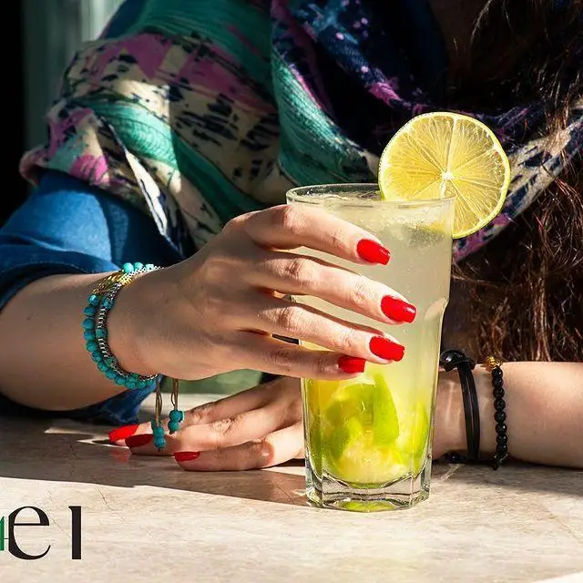 لذت نوشیدنی خنک در کافه رستوران لول ۴: دست زنی با لاک قرمز و دستبند فیروزه‌ای، لیموناد تازه را در فضایی دلنشین نگه داشته است.
