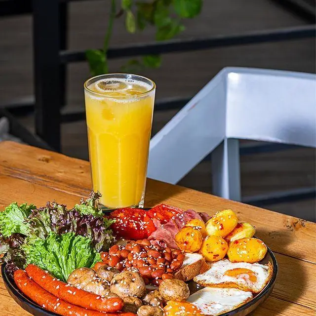 میز صبحانه لول ۴: بشقاب کامل صبحانه با نیمرو، سوسیس، لوبیا، قارچ، گوجه و سیب زمینی کنار آب پرتقال تازه و دلچسب.