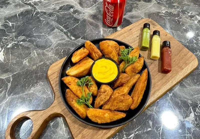 پلیت سیب‌زمینی وجز کریسپی رستوران فست فود Vee با سس دیپ زرد، سس‌های متنوع و نوشابه روی تخته چوبی. یک انتخاب عالی فست فود.