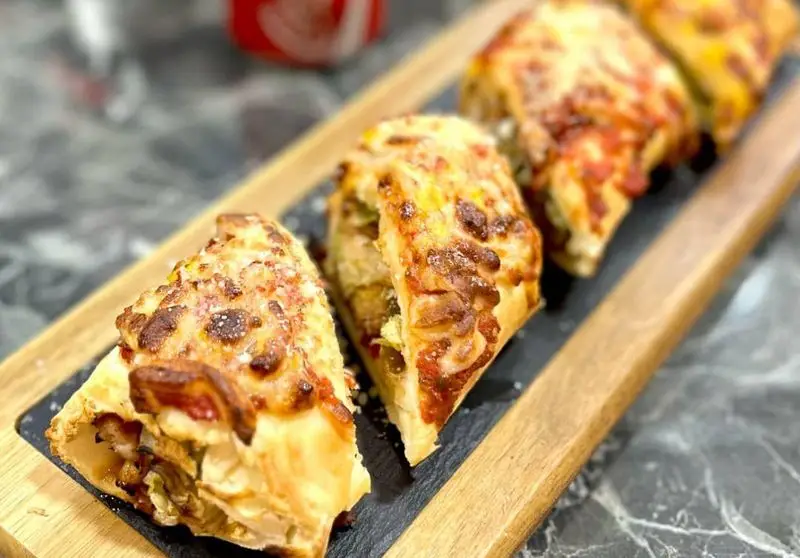 تصویری جذاب از اسلایس‌های پیتزای ویژه‌ی رستوران فست فود Vee با پنیر طلایی و لایه‌های غنی، چیده شده روی سینی چوبی شیک.