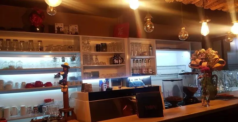 کافه ژیکو، فضای داخلی با طراحی مدرن، قفسه‌های مرتب از لیوان‌ها و فنجان‌ها، دستگاه‌های قهوه‌ساز و نورپردازی گرم، محیطی دلنشین.