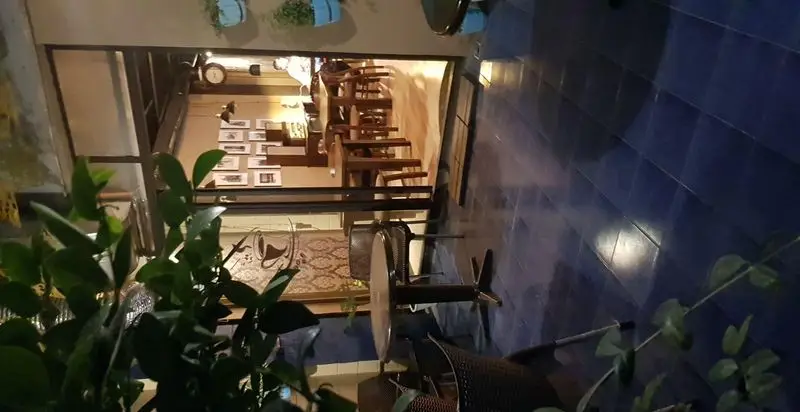 کافه ژیکو: نمایی از فضای داخلی با میز و صندلی چوبی و دکوراسیون گرم، به همراه فضای بیرونی دلنشین با کاشی‌های آبی و گیاهان سبز. محیطی آرام و ایده‌آل برای استراحت.