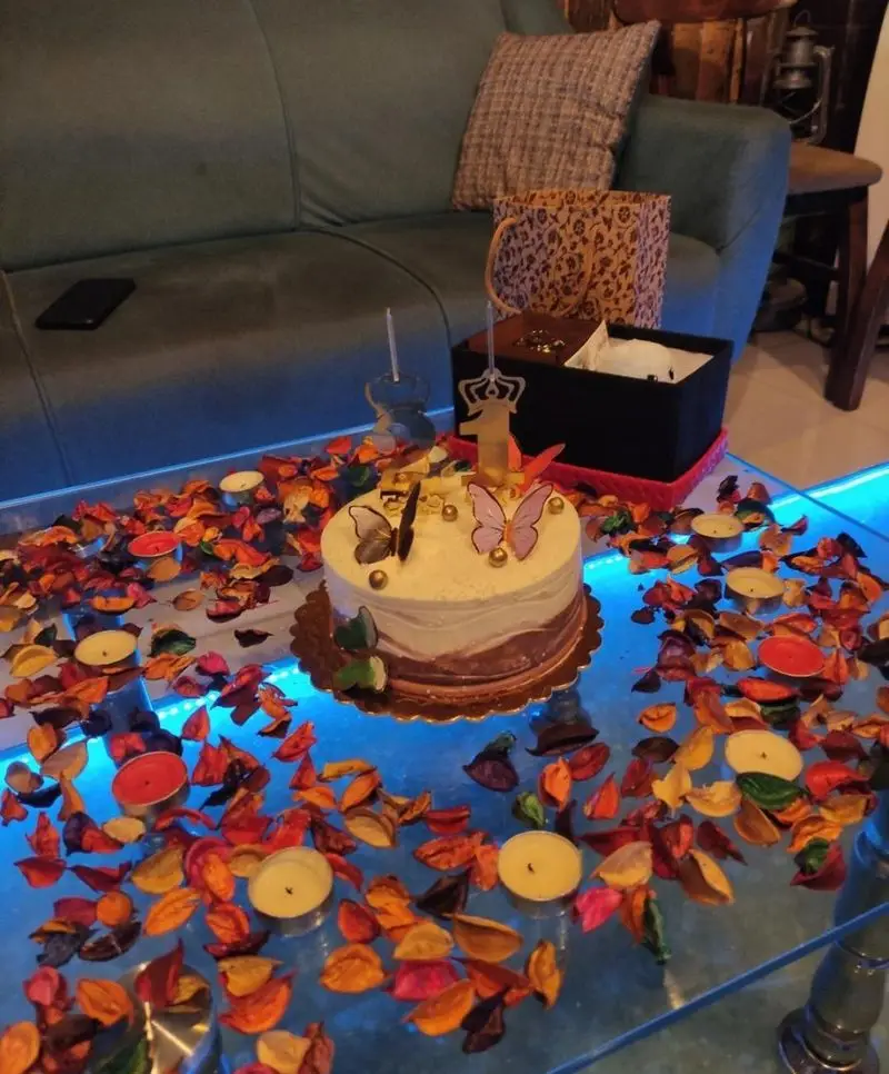 کیک تولد زیبا با شمع عدد ۱ و پروانه‌ها در کافه ژیکو، میز شیشه‌ای با شمع و برگ‌های پاییزی، فضایی رمانتیک و دلنشین.