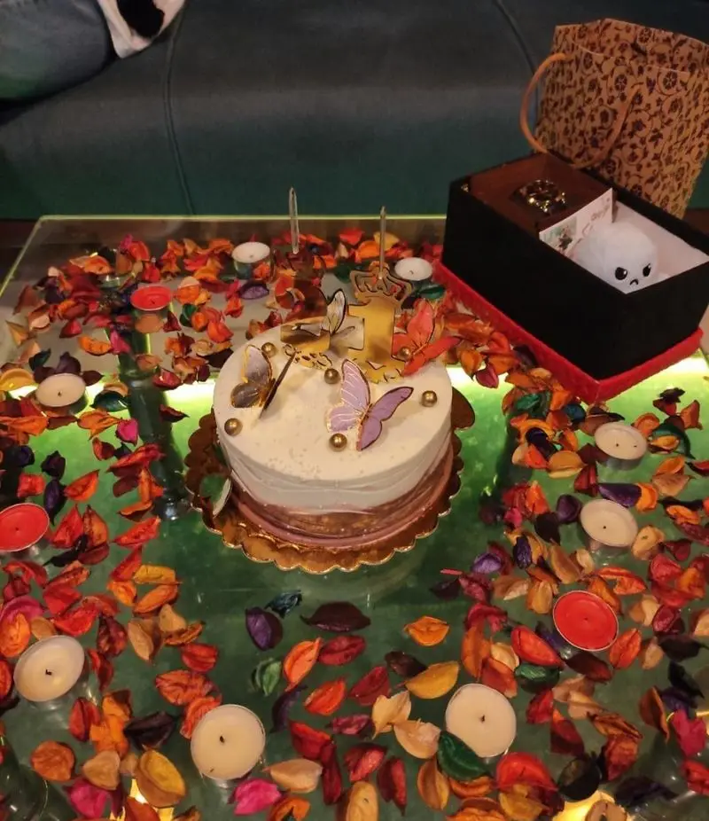تزیین رمانتیک میز در کافه ژیکو برای جشن تولد یا سالگرد با کیک پروانه، شمع، برگ خشک و هدیه؛ فضایی دلنشین برای مناسبت‌های خاص.