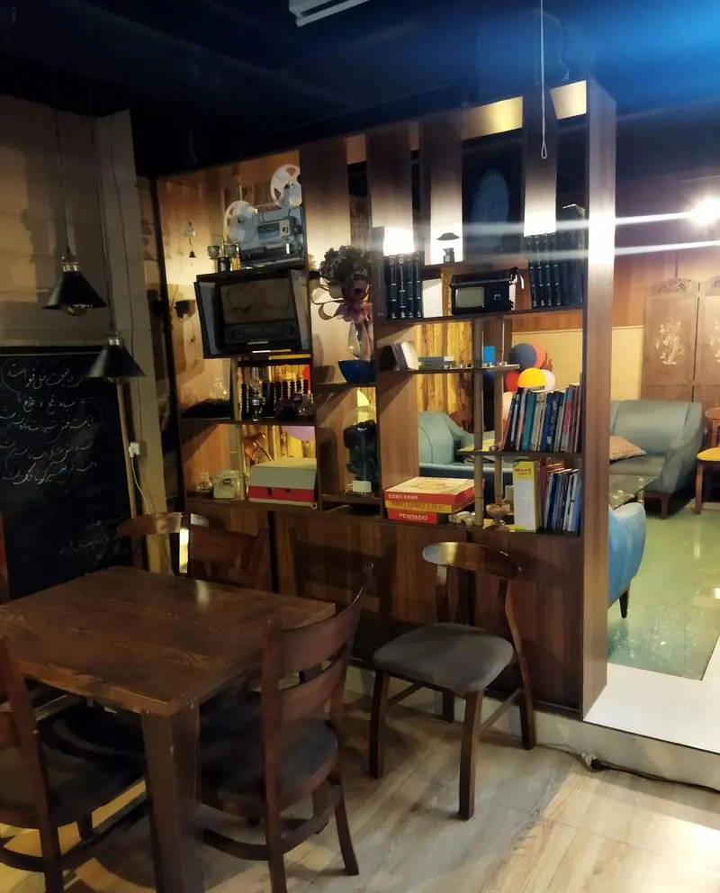 فضای داخلی دنج و دلنشین کافه ژیکو با میز و صندلی‌های چوبی، قفسه کتاب و دکوراسیون گرم برای تجربه یک کافه گردی به یادماندنی.