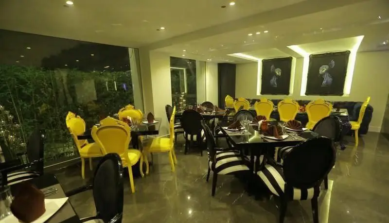 دکوراسیون داخلی شبانه کافی شاپ رینا با میز و صندلی‌های شیک زرد، مشکی و راه‌راه، فضایی لوکس و مدرن با نورپردازی دلنشین.