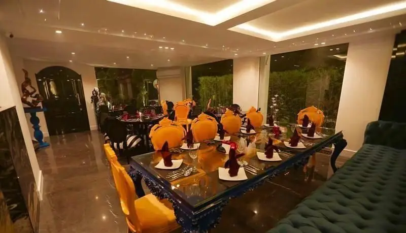 دکوراسیون داخلی مجلل کافی شاپ رینا: میز غذاخوری بزرگ با تزئینات نارنجی، صندلی‌های زرد و نورپردازی شیک، ایده‌آل برای مهمانی‌ها و جشن‌ها.