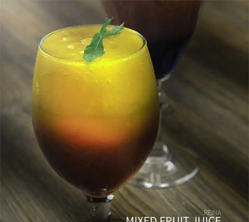 تصویری جذاب از آبمیوه مخلوط تازه و خوشرنگ با لایه‌های میوه در لیوان پایه بلند، نوشیدنی تابستانی دلچسب و خنک در کافی شاپ رینا.