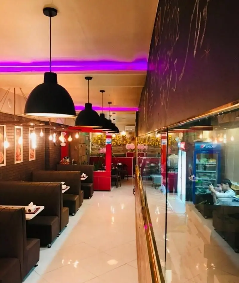 فضای داخلی کافه فست فود غذای خوب با نورپردازی بنفش و آویز، دیوارهای آجری و میز و صندلی راحت، محیطی شیک برای دورهمی و جشن.