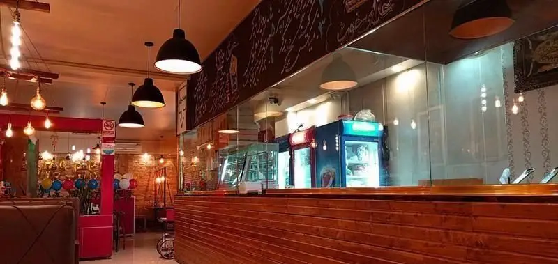 تصویری از محیط داخلی کافه فست فود "غذای خوب"، با کانتر، یخچال‌های نمایشگر و نورپردازی هنری. دکوراسیون گرم و مدرن.