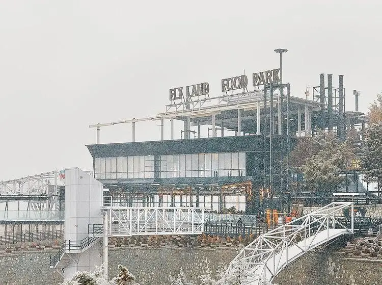 نمایی زیبا از ساختمان فلای لند فود پارک در یک روز برفی زمستانی با معماری مدرن و پل سفید در جلو.