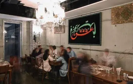 تجربه غذاخوری در روحی اکسپرس شهرک غرب: فضای داخلی شیک با لوسترهای زیبا، تابلوی خطاطی و مشتریانی در حال لذت بردن از غذا.