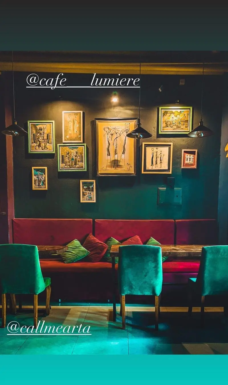 فضای داخلی کافه رستوران لومیر با دیوار سبز تیره، نقاشی، مبل قرمز، صندلی سبز مخملی و نورپردازی جذاب، محیطی دلنشین را ارائه می‌دهد.