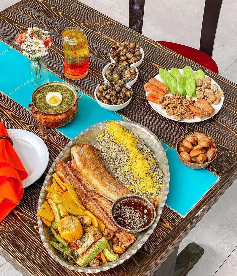 میز غذای سنتی رستوران گیلکی بهزاد شامل ماهی سفید و سبزی پلو، خورش، زیتون پرورده و سیر ترشی. عکس غذای محلی لذیذ گیلان.