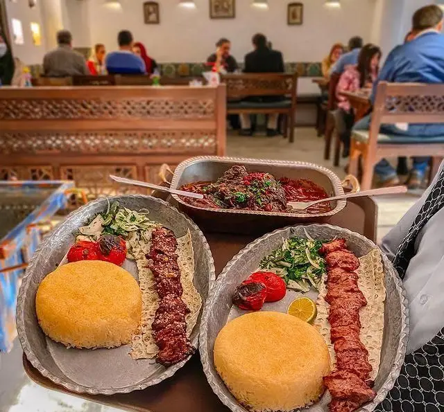 غذای اصیل و خوش طعم گیلکی شامل کباب، ته چین و خورش به همراه مخلفات در سینی‌های فلزی رستوران گیلکی بهزاد با محیطی گرم و سنتی.