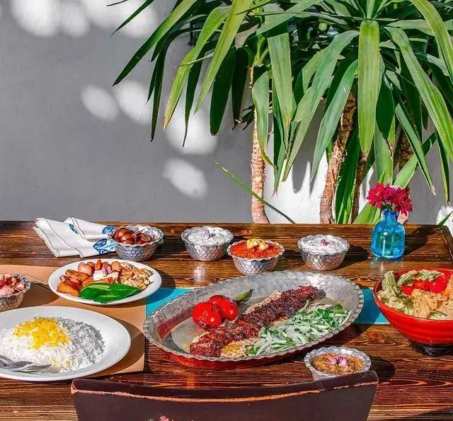 چیدمان زیبای غذا در رستوران گیلکی بهزاد شامل کباب داغ، برنج، دیپ‌ها و مخلفات گیلکی در یک محیط سرسبز و دلپذیر.