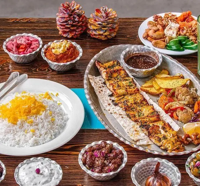 یک سفره مجلل و رنگارنگ از غذاهای رستوران گیلکی بهزاد شامل چلوکباب، برنج زعفرانی، انواع مخلفات گیلکی و ترشیجات سنتی.