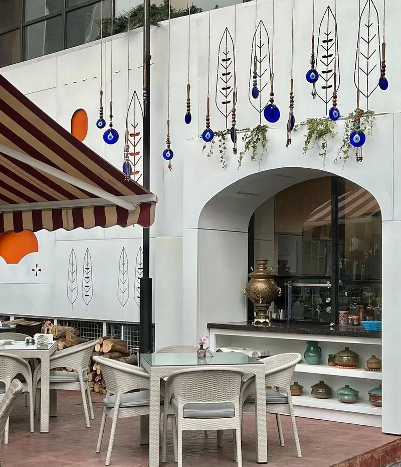 فضای بیرونی دلنشین رستوران گیلکی بهزاد با دکوراسیون سنتی، میز و صندلی حصیری، چشم‌نظر و سماور برای تجربه‌ای اصیل.