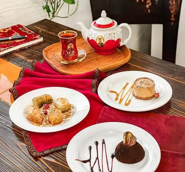 میز چای و دسرهای خاص رستوران گیلکی بهزاد، شامل باقلوا، موس شکلاتی و شیرینی‌های سنتی متنوع در فضایی دلنشین و گرم.