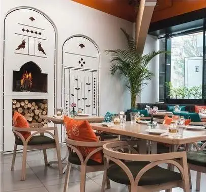 فضای داخلی دنج و دلنشین رستوران گیلکی بهزاد با دکوراسیون شیک، شامل شومینه، میز و صندلی‌های چوبی راحت و طراحی تلفیقی سنتی و مدرن.