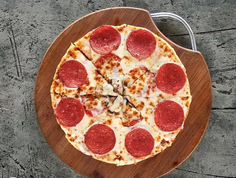 پیتزا پپرونی تازه و داغ برگرلند با پنیر فراوان و قارچ، سرو شده روی تخته چوبی. غذای عالی برای منوی فست فود.