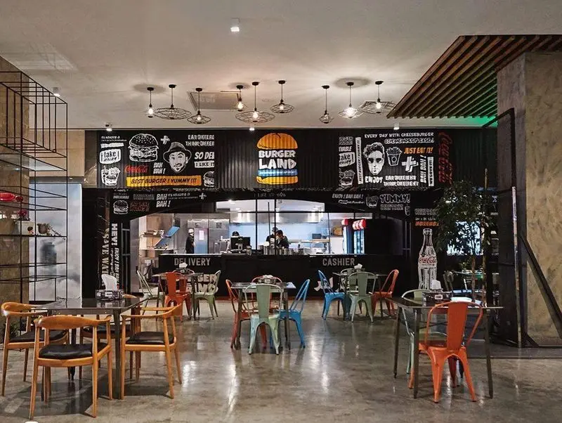 فضای داخلی شیک و مدرن رستوران برگرلند با میز و صندلی‌های رنگی، کانتر سفارش و دکوراسیون دیواری جذاب با لوگوی برگر لند و تبلیغات کوکاکولا.