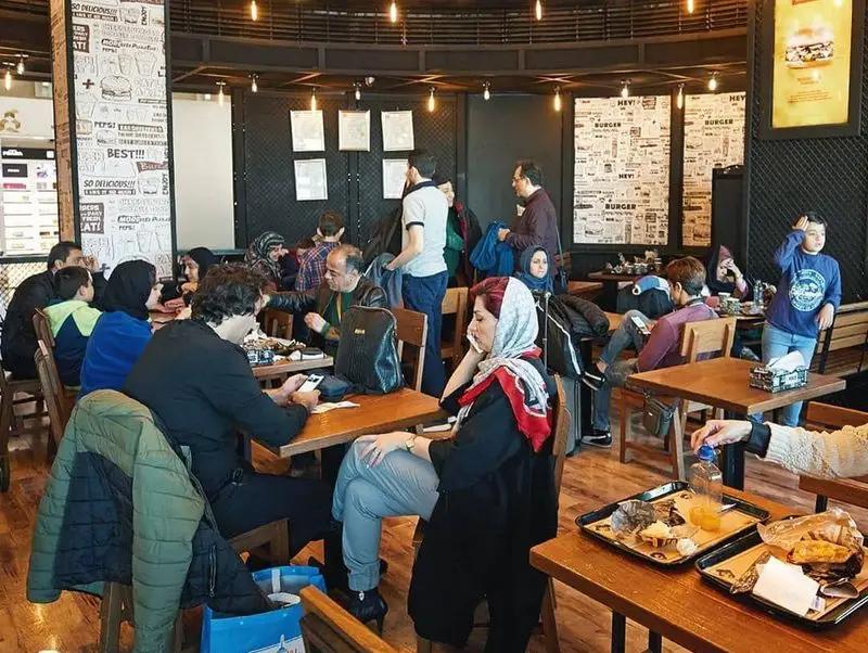 نمایی از مشتریان شاد و در حال غذا خوردن در فضای داخلی رستوران فست فود محبوب برگرلند با دکوراسیون مدرن.