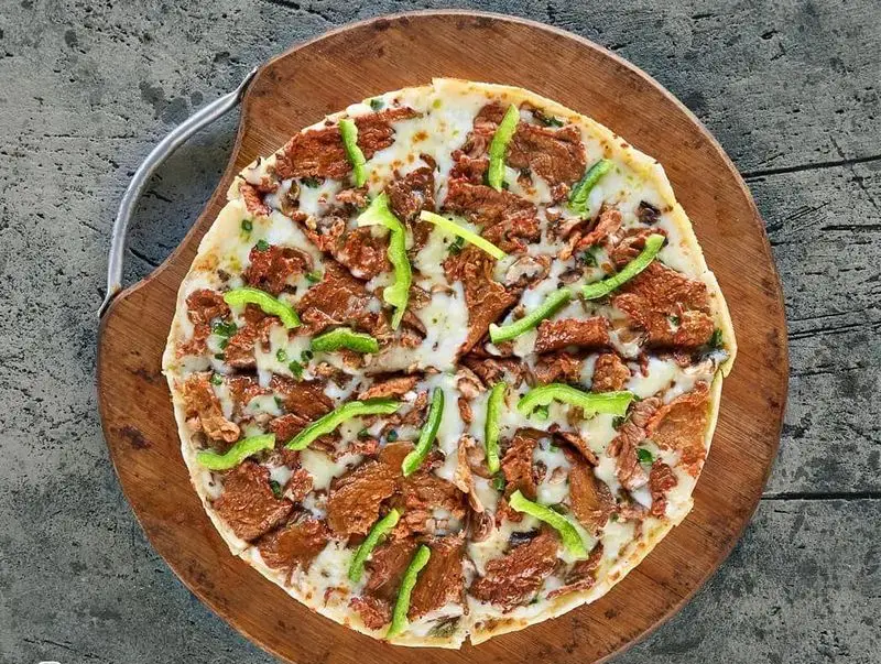 پیتزای خوشمزه گوشت و فلفل دلمه برگرلند با پنیر موزارلا، فلفل سبز و تکه‌های گوشت روی تخته چوبی مخصوص.