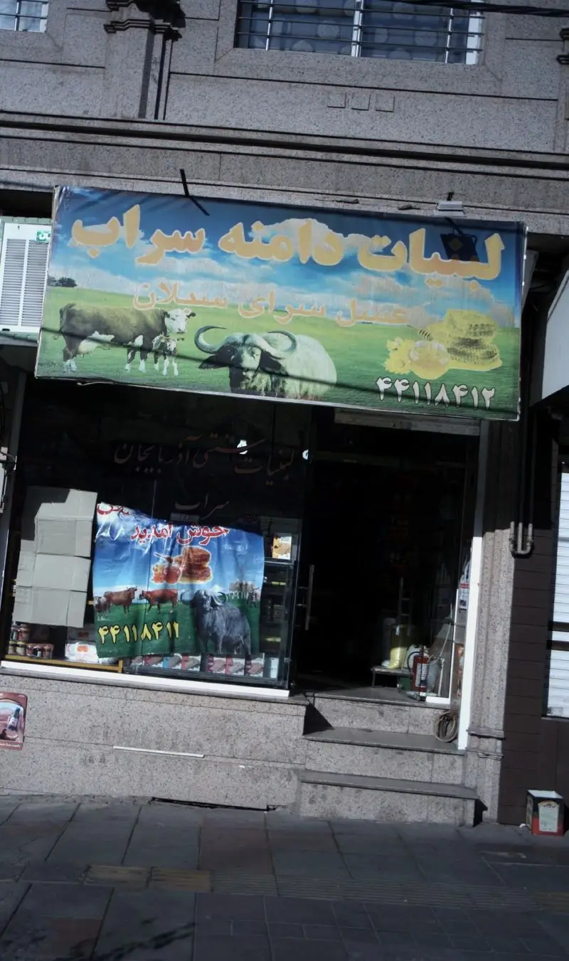 تصویری از نمای بیرونی فروشگاه لبنیات دامنه سراب با بنرهای تبلیغاتی محصولات تازه از شیر گاو و گاومیش، پنیر و عسل محلی.