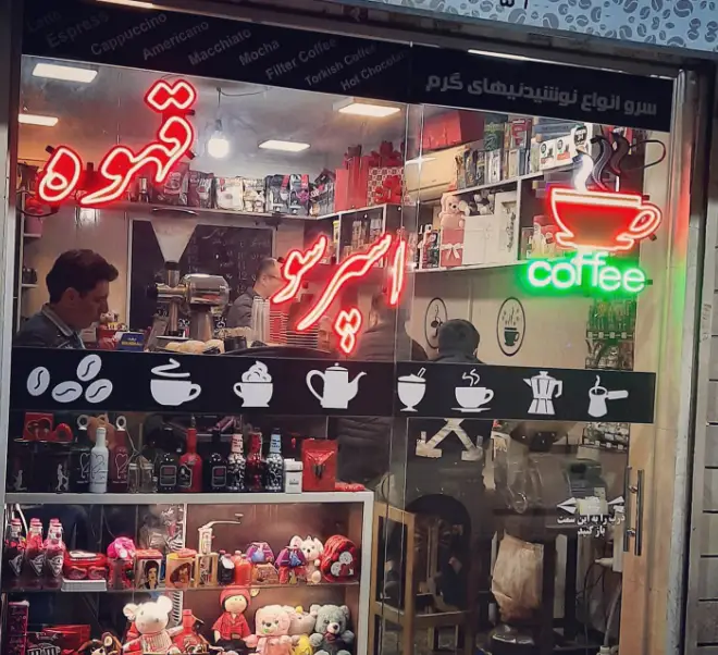 فروشگاه قهوه الی: نمای شیشه‌ای با تابلوهای نئونی قهوه و اسپرسو، نمایش منوی نوشیدنی‌های گرم و محصولات متنوع قهوه.