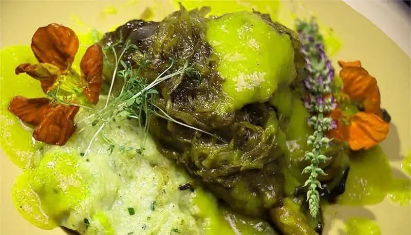 غذای خاص رستوران فرنگی ایوان برج میلاد: بشقاب سبزیجات سبز لذیذ با سس تازه، سبزیجات معطر و تزئین گل‌های خوراکی.