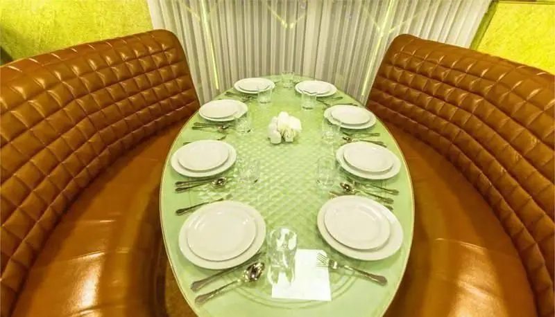 محیط داخلی رستوران فرنگی ایوان برج میلاد با میز بیضی شکل و چیدمان کامل ظروف، همراه با نیمکت‌های چرمی قهوه‌ای و دکوری شیک.