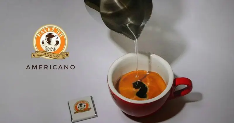 آماده سازی قهوه آمریکانو در کافی شاپ پاییز ۹۸، آب داغ به اسپرسو اضافه می‌شود. لوگوی کافی شاپ و کلمه آمریکانو.