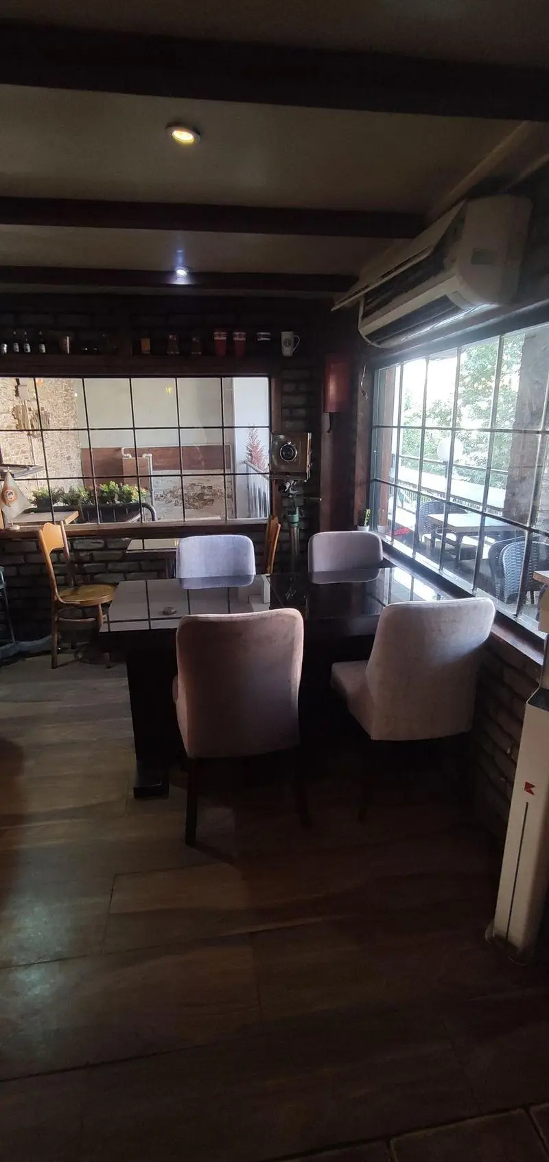 نمای داخلی دنج و دلنشین کافی شاپ پاییز ۹۸ با سقف چوبی، دیوارهای آجری، میز و صندلی‌های مدرن و پنجره‌های بزرگ رو به فضای سبز.