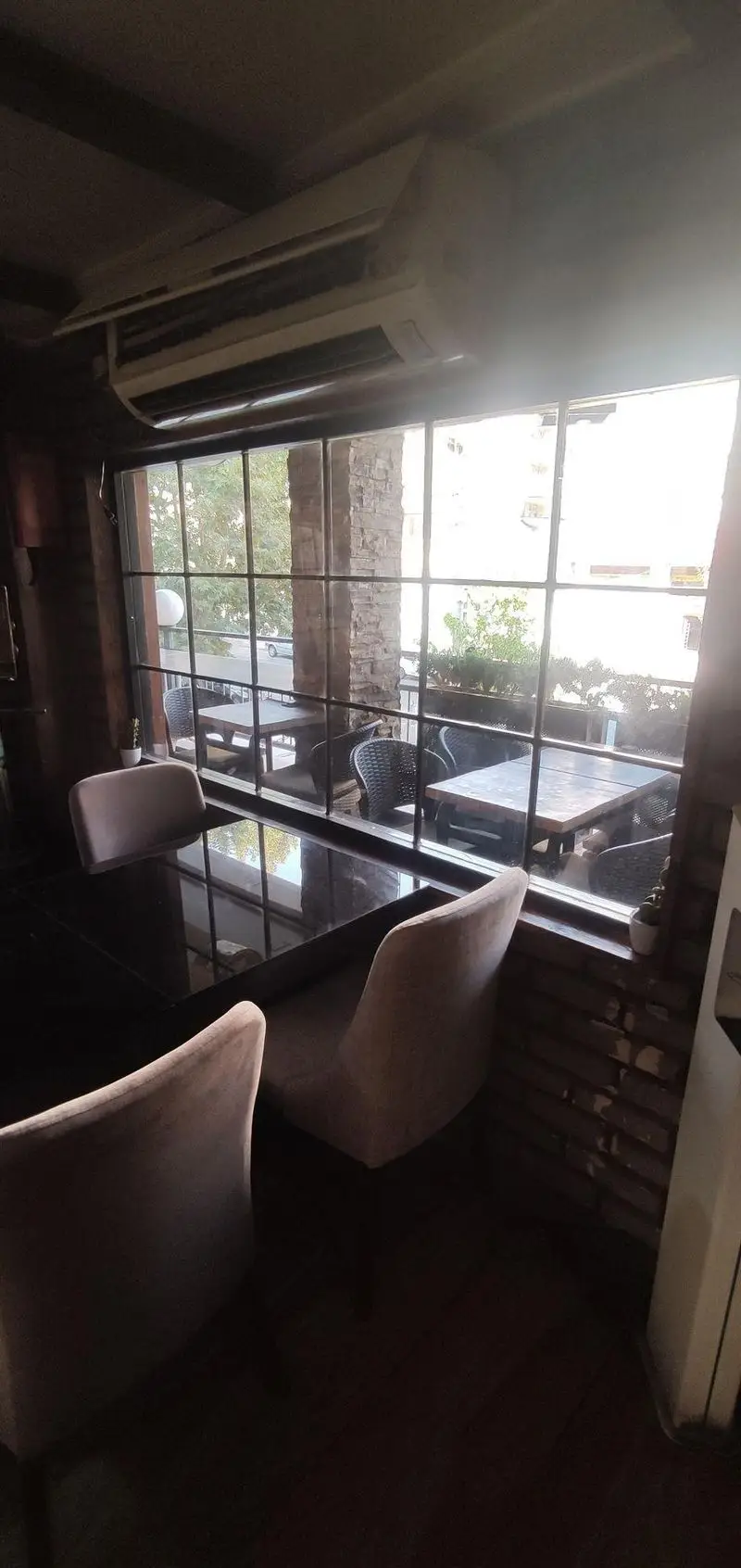 فضای داخلی دنج کافی شاپ پاییز ۹۸ با پنجره‌ای بزرگ رو به فضای سبز و میز و صندلی‌های شیک، محیطی آرامش‌بخش برای مشتریان.