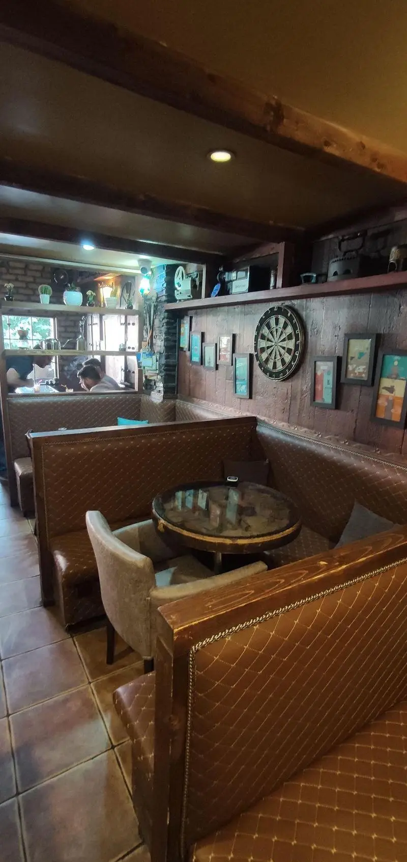 فضای داخلی دنج و گرم کافی شاپ پاییز ۹۸ با مبلمان چرمی قهوه‌ای، میزهای چوبی و دارت، ایده‌آل برای اوقات فراغت و دورهمی.