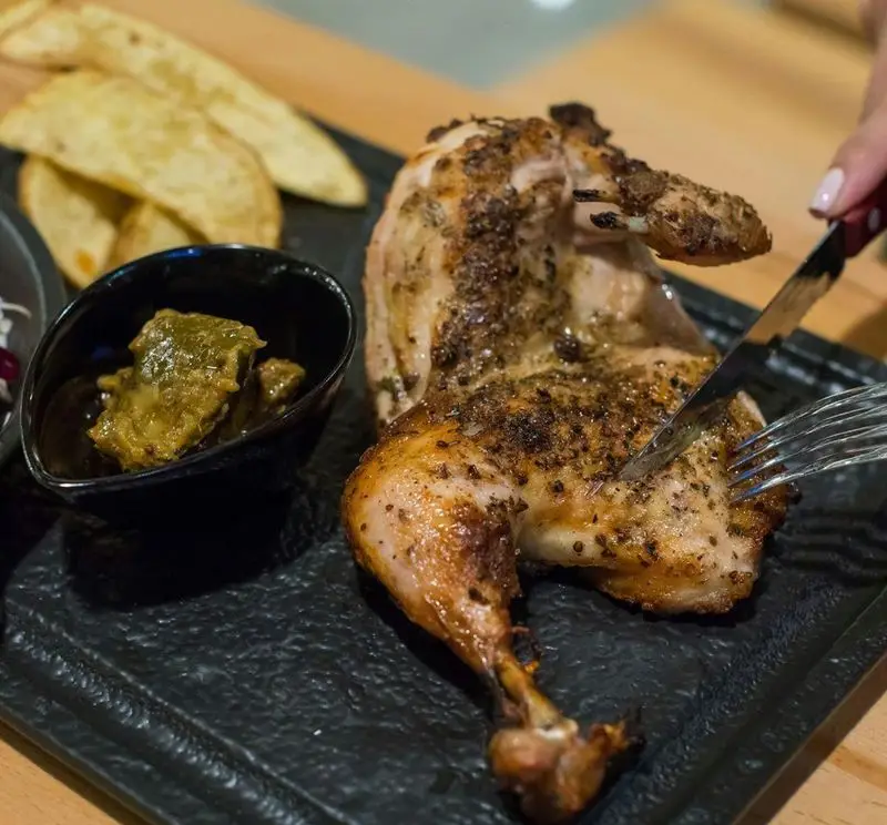 یک وعده غذایی جذاب شامل مرغ اسپچ‌کاک بریان شده با چاشنی، در حال برش، در آوافودمارکت مجتمع تجاری آواسنتر، با وجز سیب‌زمینی و سس سبز.