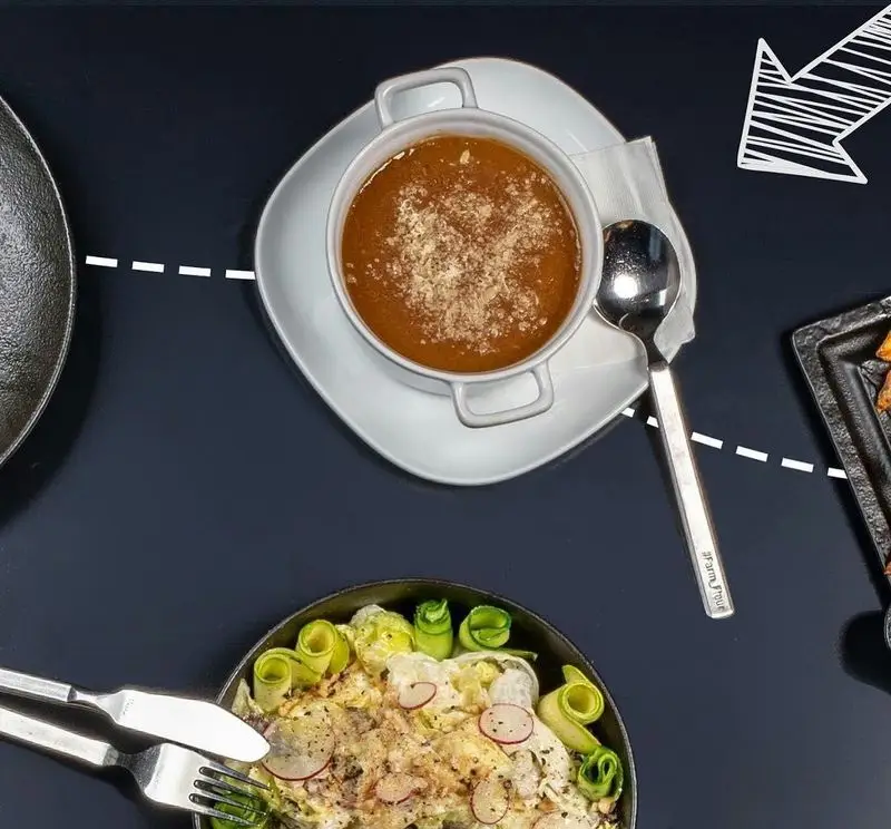 میز غذای چیده‌شده از بالا در آوافودمارکت آواسنتر: کاسه سوپ گرم با پنیر، سالاد متنوع با سبزیجات تازه و تربچه، و خوراکی‌های جانبی. تجربه لذیذ غذا.