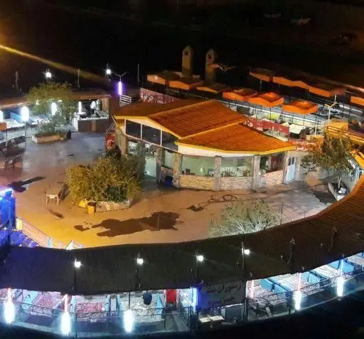 نمایی جذاب از رستوران جزیره در شب با فضای باز، سقف نارنجی، آلاچیق‌های نورپردازی شده و محیطی دلنشین برای صرف غذا.