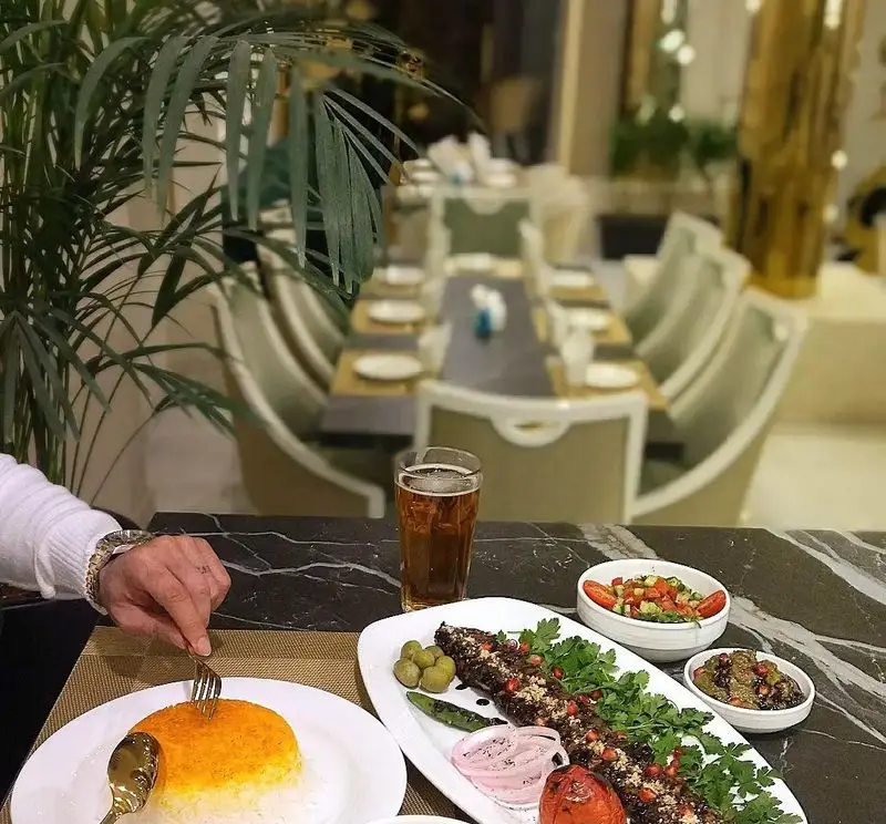 میز شیک در رستوران شاندیز روما با غذای اصیل ایرانی: کباب کوبیده، برنج زعفرانی، سالاد شیرازی و نوشیدنی خنک در فضایی مجلل.