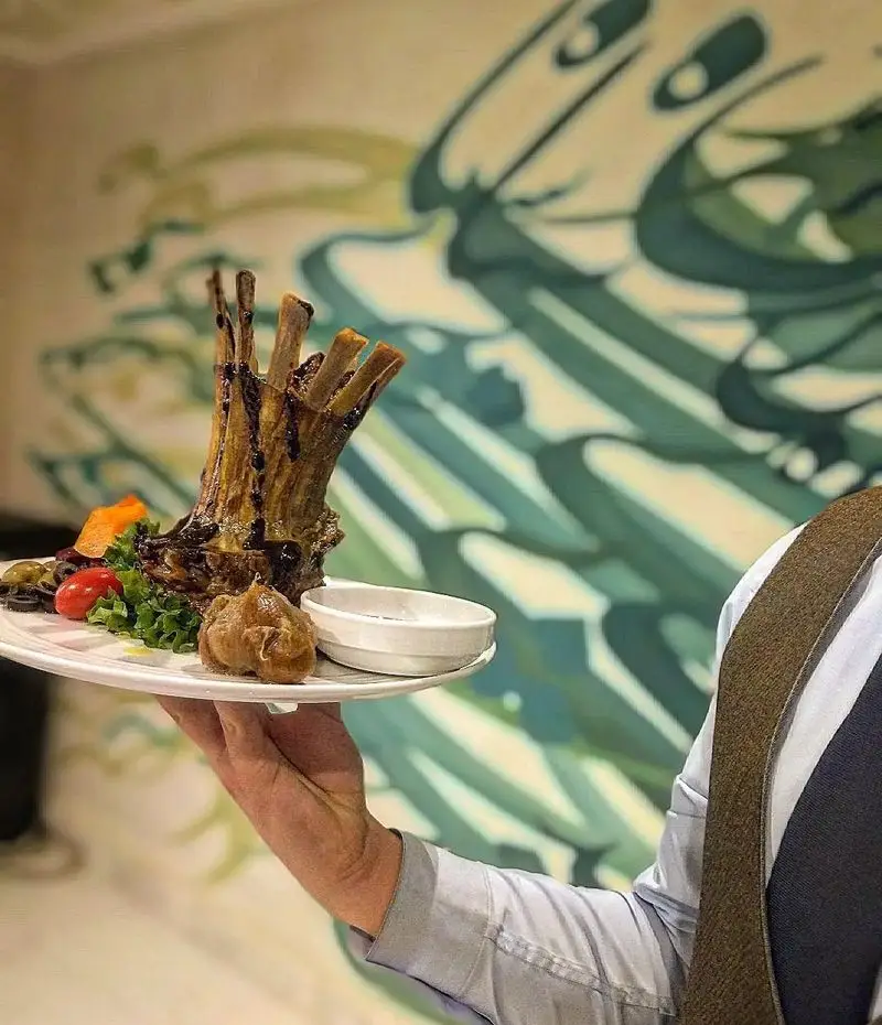 غذای ویژه و مجلل رستوران شاندیز روما: سرو شیشلیک بره آبدار با تزئینات و سس توسط پیشخدمت ماهر در محیطی چشم‌نواز.