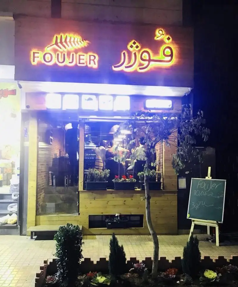 نمای بیرونی شبانه کافه رستوران فوژر با تابلوی روشن و لوگوی برگ سرخس، طراحی چوبی دلنشین، ورودی شیشه‌ای و محیطی دعوت‌کننده.